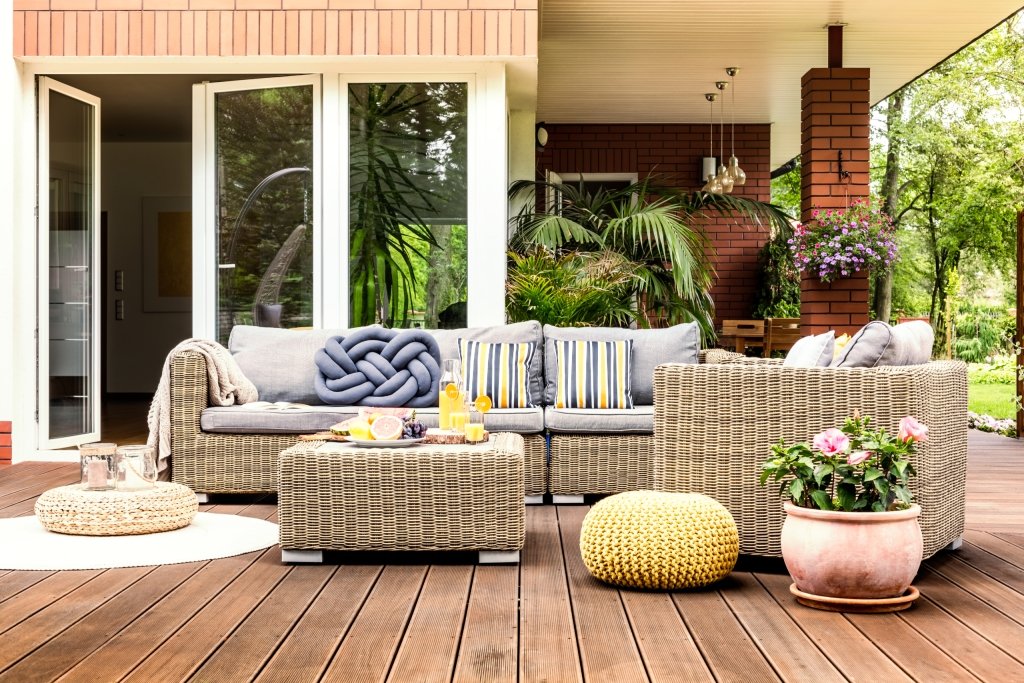 Beige garden furniture with striped pillows on a wooden terrace with pink flowers and poufs